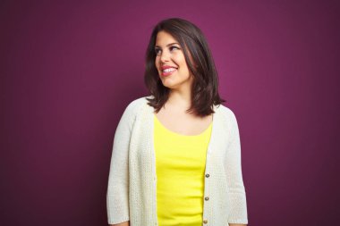 Genç, güzel, esmer bir kadın mor izole edilmiş bir arka plan üzerinde ceketi var. Yüzünde gülümseme, doğal bir ifade ile yan yana bakıyor. Kendinden emin gülen.