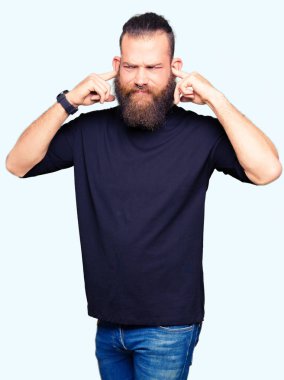 Rahat t-shirt kapsayan kulakları parmakları ile yüksek sesle müzik gürültü rahatsız ifade ile giyen genç sarışın adam. Sağır kavramı.