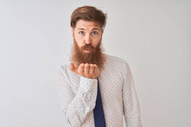 Genç kızıl saçlı İrlandalı işadamı, izole edilmiş beyaz arka planda dikilip kameraya bakarak havadan öpücükler savuruyor. Güzel ve seksi. Aşk ifadesi.