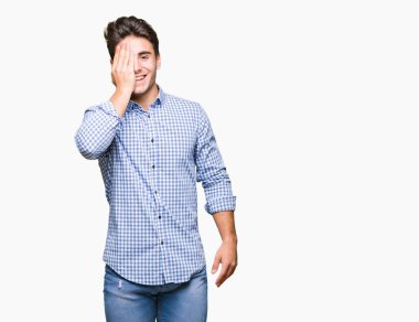 Genç yakışıklı iş adamı el yüz ve sürpriz duygu kendinden emin gülümseme ile tek gözüyle kapsayan izole arka plan üzerinde.