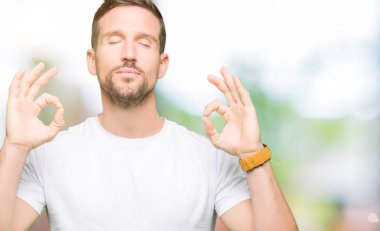 Casual beyaz t-shirt dinlenmek giydiği ve gözleri ile gülümseyen yakışıklı adam parmak ile meditasyon jest yapıyor kapalı. Yoga kavramı.