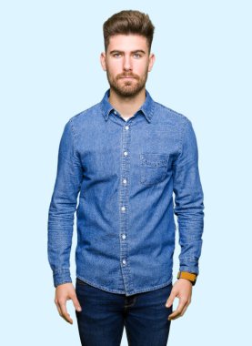 Yüzünde ciddi ifade ile gevşek rahat denim gömlek giyen genç yakışıklı sarışın adam. Basit ve doğal kameraya bakıyor.
