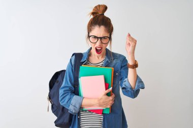 Redhead student woman wearing backpack holding books over isolated white background annoyed and frustrated shouting with anger, crazy and yelling with raised hand, anger concept