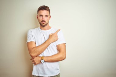 Casual beyaz t-shirt üzerinde izole giyen genç yakışıklı adam reklam, ciddi ve sakin yüz gösterilen yan el parmak ile işaret arka plan