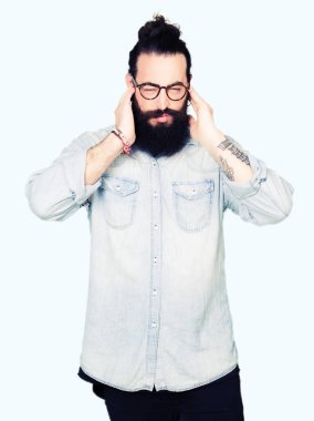 Uzun saç ve sakal kulakları ile yüksek sesle müzik gürültü rahatsız ifade parmaklarıyla kapsayan gözlüklü genç hipster adam. Sağır kavramı.