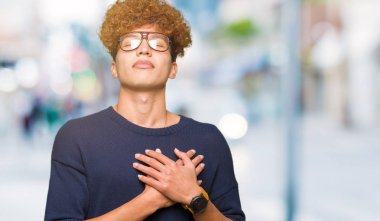 Afro gözlük ile gülümseyen genç yakışıklı adamla kapalı gözler ve yüzünde minnettar jest ile göğüs üzerinde eller. Sağlık kavramı.