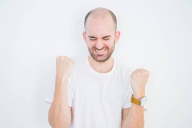 Genç ve kel bir adam beyaz arka planda mutlu ve heyecanlı bir şekilde kollarını kaldırıp, gülümseyip, başarı için haykırıyor. Kutlama konsepti.