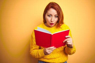 Sarı arka plan üzerinde kırmızı kitap okuyan genç bir kızıl saçlı öğretmen. Şaşırmış bir yüzle korkmuş ve korku ifadesinden korkmuş.