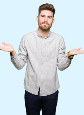 Sıradan gömlekler giyen, elleri ve kolları havada, kafası karışmış genç yakışıklı bir adam. şüphe kavramı.