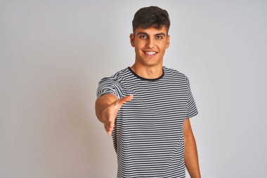 İzole edilmiş beyaz arka planda duran donanma çizgili tişört giyen genç Hintli adam dostça bir selamlama ve hoş geldin hediyesi olarak el sıkışmayı sunuyor. Başarılı bir iş..