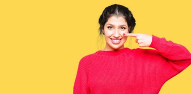 Kırmızı kazak ve topun giyen genç güzel kadın yüz ve burun el parmağı ile işaret, neşeli gülümseyen