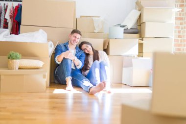 Evde karton kutular etrafında yerde oturan rahatlatıcı genç güzel çift, yeni bir eve hareket mutlu gülümseyen