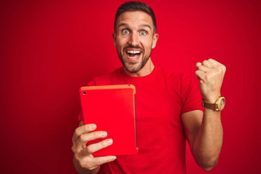 Genç adam kırmızı arka plan üzerinde dijital dokunmatik tablet kullanıyor. Gururla bağırıyor, zaferi ve başarıyı kutluyor. Çok heyecanlı, coşkulu bir duygu.
