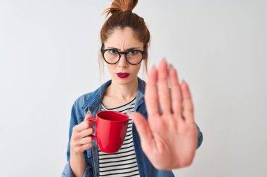Young beautiful redhead woman drinking cup of coffee over isolated white background with open hand doing stop sign with serious and confident expression, defense gesture