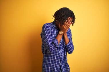 Rastgele gömlek giyen Afro bir adam izole edilmiş sarı arka planda dikiliyor ve ağlarken suratını ellerle kapatıyor. Depresyon kavramı.