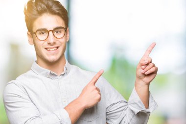 Gülümseyen ve iki elleri ve parmakları ile tarafına işaret kamera bakarak izole arka plan üzerinde gözlük takan genç yakışıklı adam.