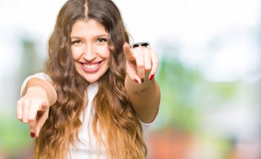 Olumlu ve neşeli gülümseyen casual beyaz t-shirt işaretleme ve parmaklar, kamerayla giyen genç güzel kadın