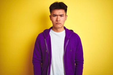Mor kazak giyen Asyalı genç adam izole edilmiş sarı arka plan üzerinde duruyor şüpheci ve gergin, sorun yüzünden surat asıyor. Negatif kişi.