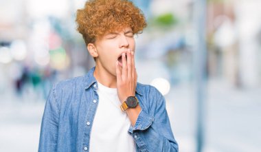 Afro saçlı kot ceket giyen genç yakışıklı adam el ağzıyla kapsayan yorgun esneme sıkılmış. Restless ve uyku hali.