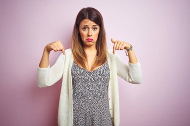 Pembe soyutlanmış arka planda duran genç ve güzel bir kadın üzgün ve üzgün görünüyor, parmaklarıyla yönü gösteriyor, mutsuz ve depresif..