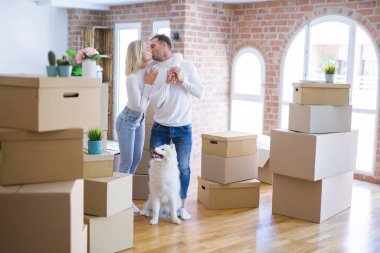 Karton kutular etrafında yeni evde ayakta köpek öpüşme ile genç güzel çift