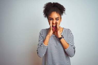 Siyah çizgili tişört giyen Afro-Amerikalı bir kadın izole edilmiş beyaz arka planda duruyor ve elleri ağzında kızgın bir şekilde bağırıyor.