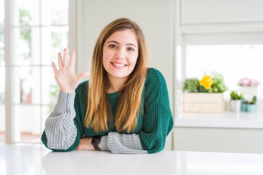 Güzel, iri yarı, sıradan çizgili süveter giyen genç bir kadın beş numaralı parmaklarıyla işaret ederken kendine güvenen ve mutlu bir şekilde gülümsüyor..