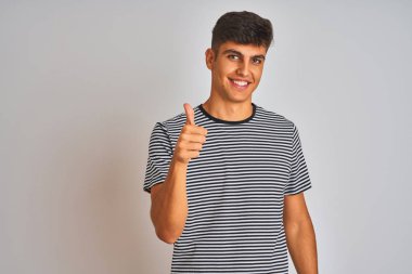 İzole edilmiş beyaz arka planda duran, donanma çizgili tişört giyen genç Hintli adam elleriyle mutlu bir jest yapıyor. Kameraya bakıp başarıyı gösteren ifade onaylanıyor.