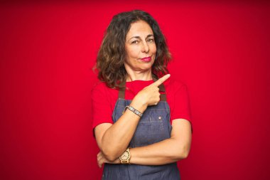 Kırmızı yalıtılmış arka planda önlük giyen orta yaşlı bir kadın. El ile işaret ederek reklamı gösteriyor. Ciddi ve sakin bir yüz.