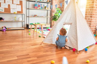 Renkli oyun odasında beyaz güzel bir bebek oyuncaklarla oynuyor. Anaokulundaki Kızılderili çadırında mutlu ve eğlenceli..