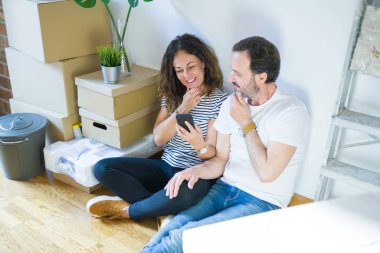 Orta yaşlı çift yeni bir eve taşınıyor. Akıllı telefon kullanıyor. Ciddi yüz ifadeleri kullanıyor.