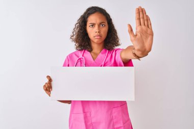 Genç Brezilyalı hemşire beyaz arka planda pankart tutuyor. Açık elle dur işareti yapıyor. Ciddi ve kendinden emin bir ifadeyle, savunma jesti.