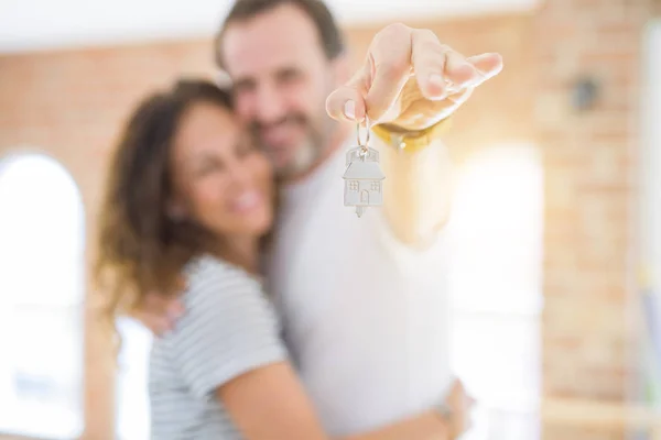 Middle age senior romantic couple holding and showing house keys, hugging and smiling happy for moving to a new home