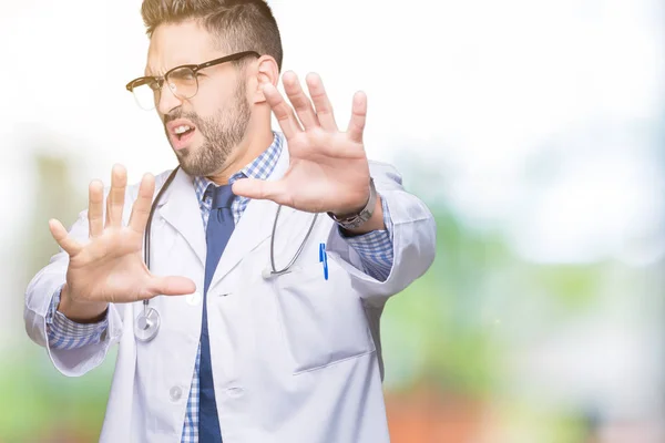 Handsome young doctor man over isolated background afraid and terrified with fear expression stop gesture with hands, shouting in shock. Panic concept.