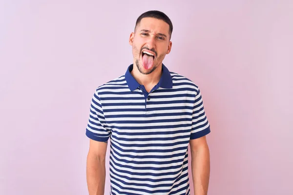 年轻英俊的男子穿着航海条纹T恤 穿着粉色孤立的背景 带着滑稽的表情伸出舌头 情感概念 — 图库照片