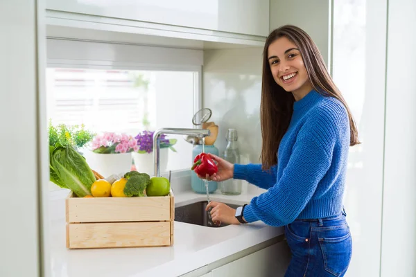 Young woman washing vegetables and fruit using water from sink