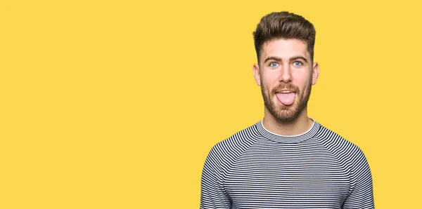 年轻英俊的男人穿着条纹毛衣伸出舌头出来愉快的搞笑的表情 情感概念 — 图库照片