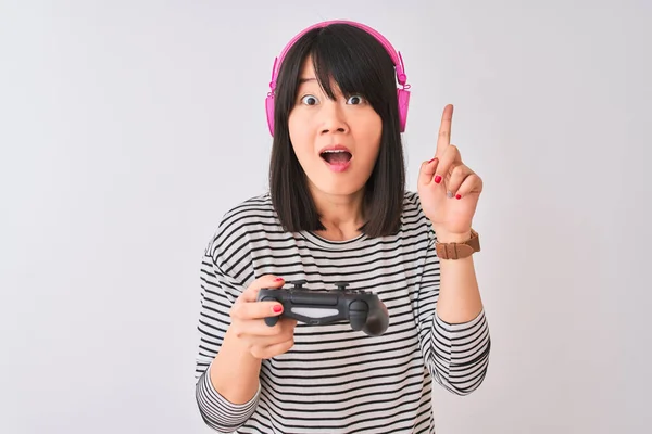 中国玩家妇女玩视频游戏使用耳机在孤立的白色背景惊讶与想法或问题指向手指与快乐的脸 — 图库照片