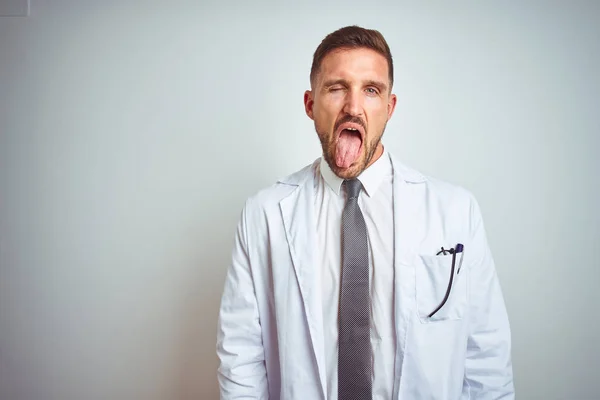 楽しそうな表情で幸せそうに舌を突き出す孤立した背景に白いプロのコートを着た若いハンサムな医者男 感情概念 — ストック写真