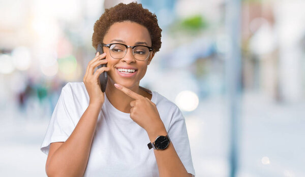 Молодая африканская американка, разговаривающая по телефону на изолированном фоне, очень довольна, указывая рукой и пальцем.
