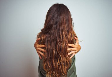 Yeşil tişörtlü genç ve güzel bir kadın, gri izole arka planda dikiliyor. Kendine mutlu ve pozitif bir şekilde sarılıyor. Sevgi ve özgüven.