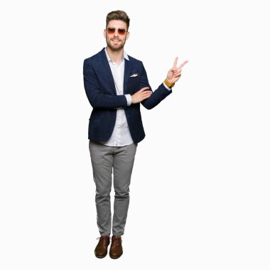 Güneş gözlüğü ve mutlu yüz zafer işareti yaparken kameraya göz kırpıyor ile gülümseyen moda ceket giyen genç yakışıklı zarif adam. İki numaralı.