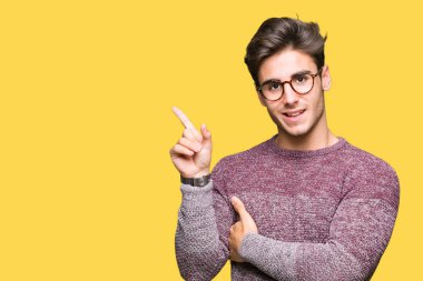 Kameraya bakarak yan el ve parmak ile işaret yüzünde kocaman bir gülümseme ile izole arka plan üzerinde gözlük takan genç yakışıklı adam.