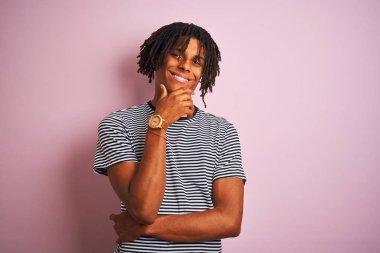 Rasta saçlı, donanma çizgili tişörtlü bir Afro adam izole edilmiş pembe arka planda dikiliyordu. Kameraya kollarını kavuşturmuş ve çenesine kaldırmış şekilde gülümsüyordu. Olumlu düşünüyorum..