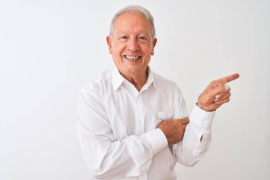 Yaşlı, gri saçlı, zarif gömlekli adam izole edilmiş beyaz arka planda duruyor. Yüzünde kocaman bir gülümseme var. Eli ve parmağı kameraya bakıyor..