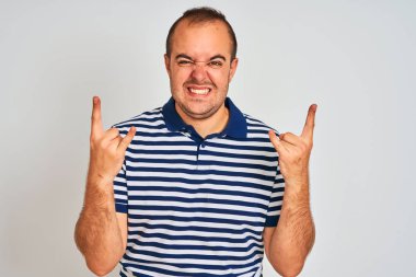 Sıradan çizgili polo giyen genç adam izole edilmiş beyaz arka planda durup çılgın bir ifadeyle elleri havada rock sembolü yaparak bağırıyor. Müzik yıldızı. Ağır müzik konsepti.