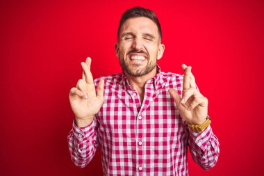 Kırmızı izole edilmiş arka plan üzerinde genç yakışıklı adam umut ve gözlerin kapalı bir şekilde gülümseyerek bana işaret ediyor. Şans ve batıl inanç..