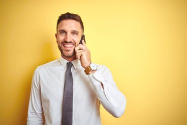 Genç yakışıklı iş adamı telefonda konuşuyor, sarı izole edilmiş arka planda. Mutlu bir yüzü var. Kendine güvenen bir gülümsemeyle dişlerini gösteriyor.