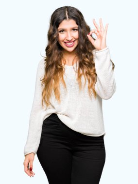 El ve parmak ile ok işareti yapıyor olumlu gülümseyen beyaz kazak giyen genç güzel kadın. Başarılı ifade.