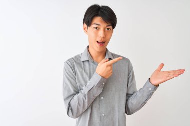 Soyutlanmış beyaz arka plan üzerinde duran zarif gömlek giyen Çinli işadamı kameraya hayret ediyor ve gülümsüyor..